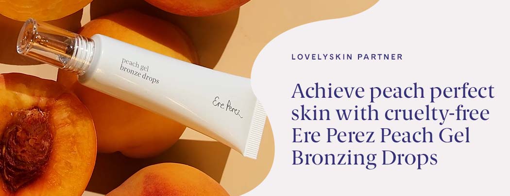 A tube of Ere Perez Peach Gel Bronzing Drops lays over peaches. Some are cut open and some are whole.