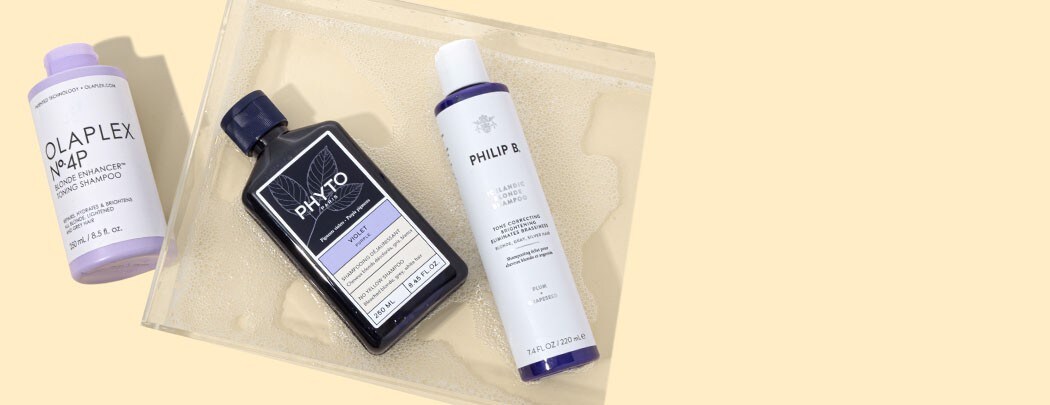 Bottles of purple shampoo from OLAPLEX, PHYTO and Philip B. on a beige background.