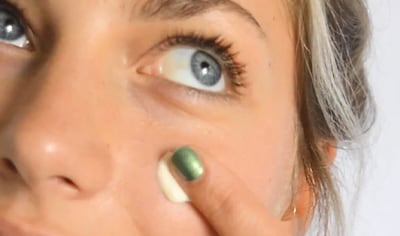 A woman with fair skin and blue eyes presses a dollop of Ere Perez Moringa All Beauty Cream into her cheek.
