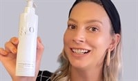 A woman with blonde hair holding up a bottle of cleanser.