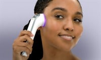 A woman with a deep skin tone and dark brown hair applies the Althaea Skin CARA Multi-Modal Tool to her face.
