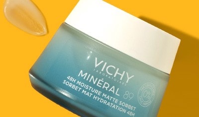 A light blue glass jar of Vichy Mineral 89 48H Moisture Matte Sorbet moisturizer on an orange background.