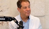 A dermatologist in a doctor's coat smiling in front of a podcast microphone.