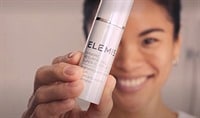 A woman holding a white tube of ELEMIS Dynamic Resurfacing Super C in front of her face at an angle.