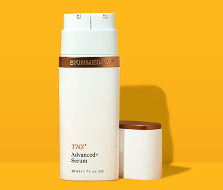 A white bottle with bronze details that reads "TNS Advanced+ Serum" stands on a yellow background.