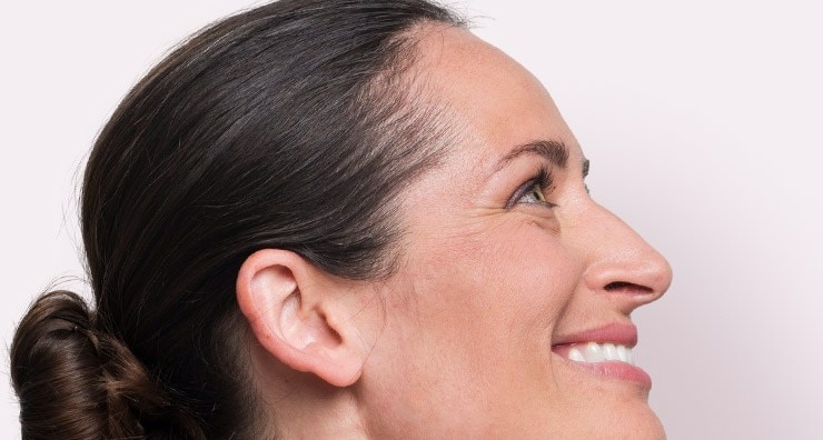 A light-skinned brunette model in profile, smiling with hair styled in a bun.