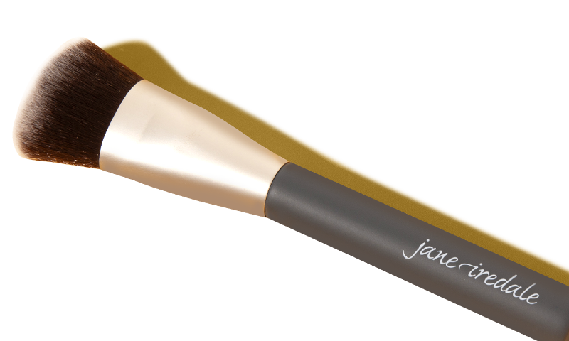A Laura Geller contour brush with the cap off so that the white-tipped bristles are visible.