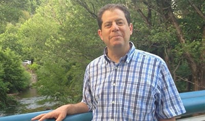 Dr. Joel Schlessinger stands over a stream while smiling.