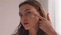 A woman with curly red hair applying a swatch of white ELEMIS Marine Cream SPF 30 across her cheek with her fingertip.