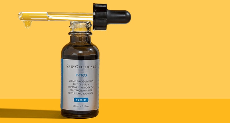 A bottle of SkinCeuticals P-TIOX serum with a dropper sitting on top on an orange background