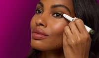 A black woman applying an eyeshadow stick to her eyelid and looking into the distance.