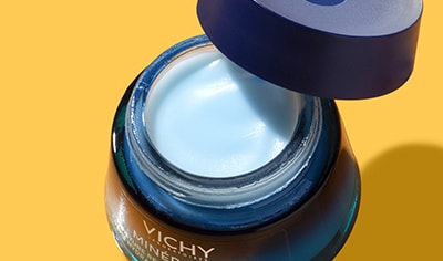 A glass pot of Vichy Mineral 89 Moisture Recovery Night Cream with lid removed and askew pictured on an orange background.