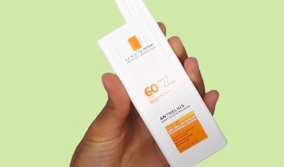 A hand with medium skin tone holds a white bottle of La Roche-Posay Anthelios 60 Ultra Light Sunscreen Fluid SPF 60
