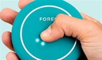 A hand with a light to medium skin tone holds the evergreen FOREO BEAR 2 body device as it lights up