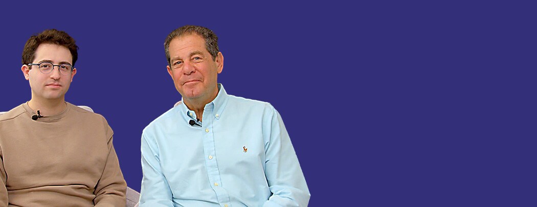 Two men, one with dark brown hair and one with light brown hair, sit next to one another.