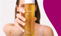 A woman with olive toned skin and brown hair holds a marigold-colored bottle of Jurlique Calendula Toner.