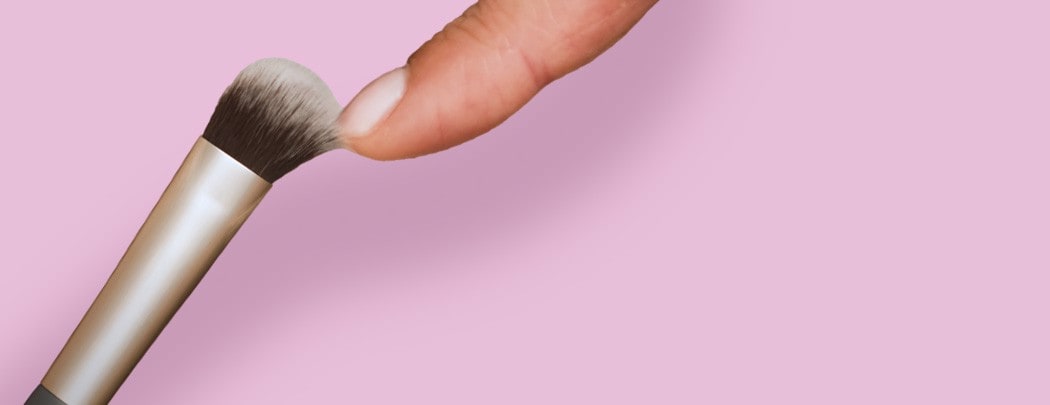 A finger tip touching the bristles of a jane iredale Concealer Brush