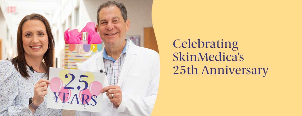 A woman and a man in a white doctor's coat smiling and  holding up a sign that says 25 years with pink and yellow balloons.