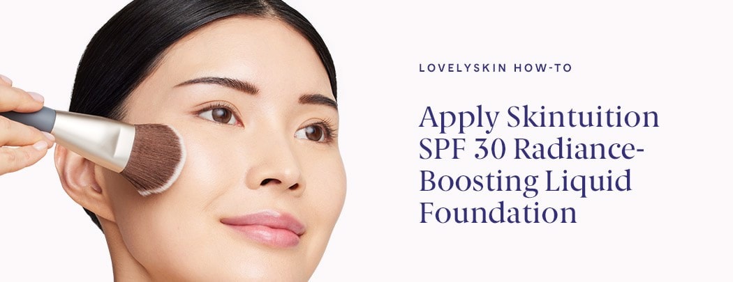 A woman of asian descent with dark brown hair and brown eyes smiles while pressing a makeup brush onto her cheek.