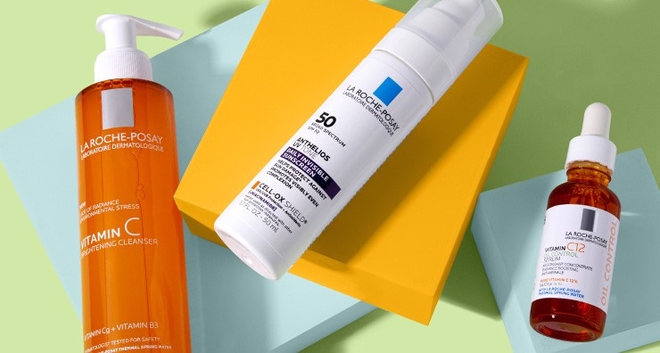 Bottles of La Roche-Posay cleanser, sunscreen and vitamin C serums laying on pastel blue and bright orange blocks on a light green background.