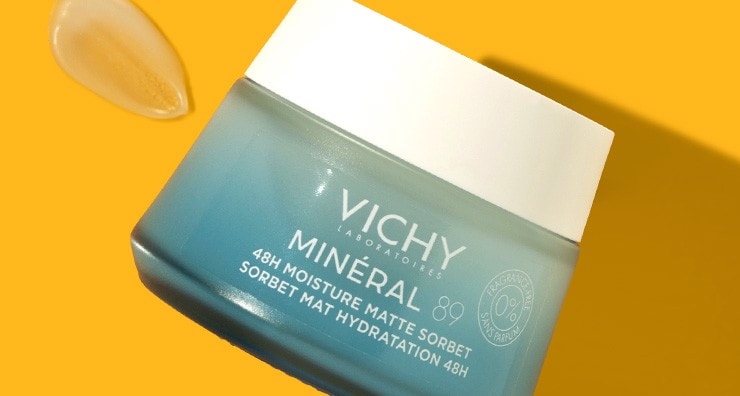 A light blue glass jar of Vichy Mineral 89 48H Moisture Matte Sorbet moisturizer on an orange background.