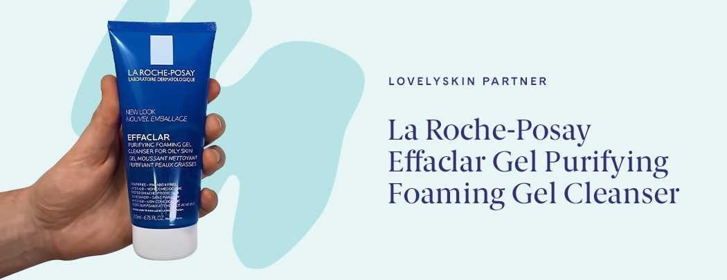 hand holding dark blue bottle of La Roche-Posay Purifying Face Wash on light blue background with darker blue illustrative element