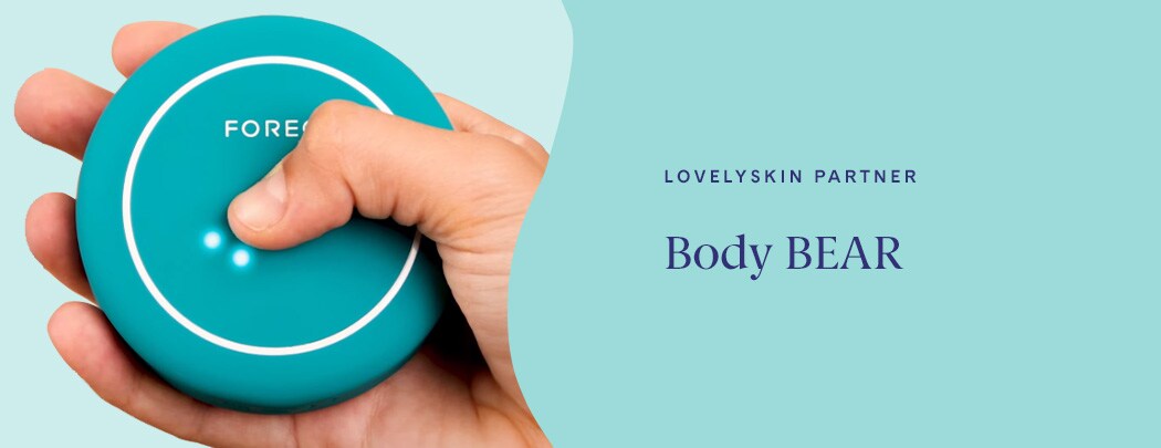 A hand with a light to medium skin tone holds the evergreen FOREO BEAR 2 body device as it lights up