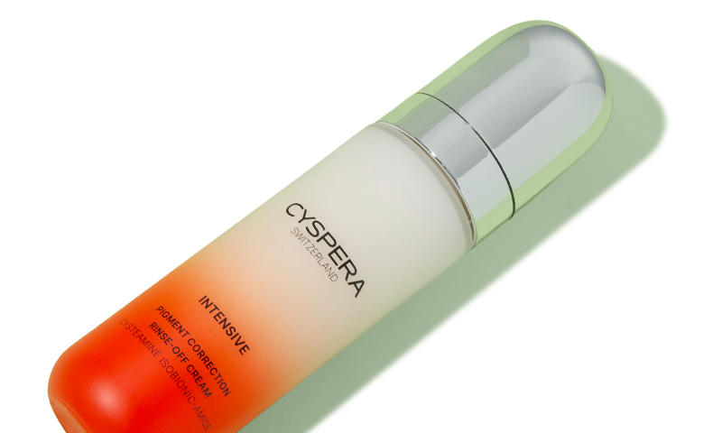 Bottle of Cyspera Intensive Pigment Correction Rinse-Off Cream on a light green background, angled diagonally