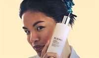 An asian woman holding a bottle of ELEMIS Dynamic Resurfacing Face Wash close to her cheek.