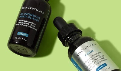 Dark brown glass serum bottles of SkinCeuticals P-TIOX and HA Intensifier Multi-Glycan placed diagonally on a light green background.